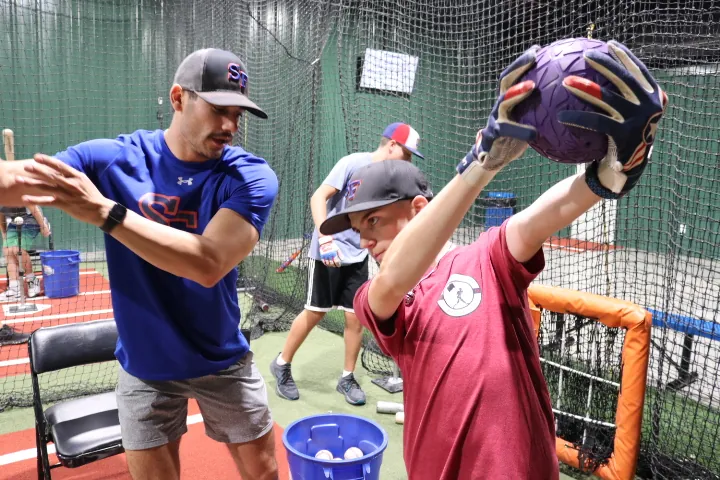 A coach working a young player through a throwing drill in a batting cage